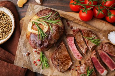 Pieces of delicious beef meat, spices and tomatoes on wooden table, flat lay