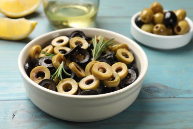 Farklı lezzetlerde marine edilmiş zeytin halkaları ve biberiye açık mavi ahşap masada, yakın plan.