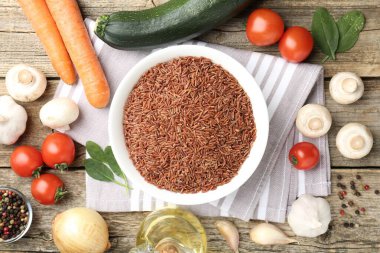 Tabaktaki çiğ kahverengi pirinç taze ürünlerin arasında, ahşap masada, düz yerde.