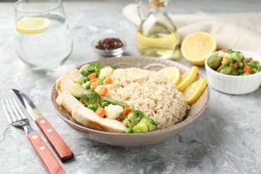 Gri desenli masada servis edilen tavuk, sebze ve limon dilimleri ile nefis kahverengi pirinç, yakın plan.