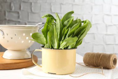 Beyaz masada taze kuş yaprakları, sicim ve kevgir.