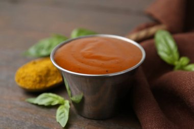 Lezzetli köri sosu metal tabakta, toz ve fesleğen ahşap masada, yakın plan.