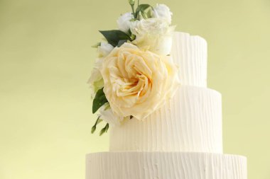 Açık yeşil arka planda çiçeklerle süslenmiş lezzetli düğün pastası, yakın plan.