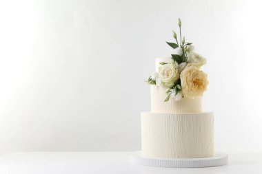 Masada beyaz arka planda çiçeklerle süslenmiş nefis bir düğün pastası. Metin için boşluk