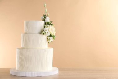 Ahşap masadaki çiçeklerle süslenmiş nefis düğün pastası bej arka planda, yakın plan. Metin için boşluk