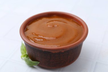 Lezzetli köri sosu ve fesleğen yaprakları beyaz fayanslı masada, yakın plan.