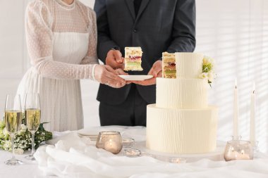 Damat, düğün pastasından bir parça tabağa koyuyor. Gelini masada kapalı tutuyor, yakın plan.