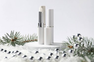 Nemlendirici dudak kremleri, Noel dekorasyonu ve beyaz arka planda suni kar üzerindeki köknar ağacı dalları, yakın plan. Kış bakımı