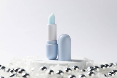 Nemlendirici dudak kremi ve yapay kar üzerindeki Noel süsü beyaz arka planda, yakın plan. Kış bakımı