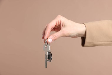 Emlakçının elinde anahtarlık bej arka planda ev şekilli anahtarlık, yakın plan.