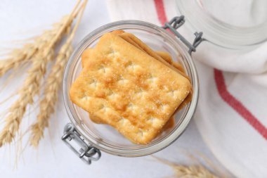 Lezzetli tuzlu krakerler ve buğday başakları beyaz masada, düz yerde.