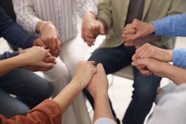 Grup psikoterapi seansı sırasında el ele tutuşan insanlar kapalı mekanda, yakın çekim