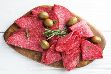 Beyaz ahşap masada servis edilen zeytinli ve biberiyeli lezzetli sosis dilimleri.