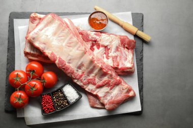 Çiğ domuz kaburgası, domates ve baharatlar gri masada.