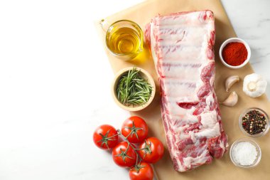 Çiğ domuz kaburgası, baharatlar ve domatesler beyaz masada, düz yayılmış. Metin için boşluk