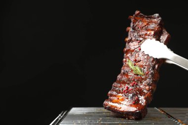 Siyah arka planda ızgaradan maşayla leziz domuz pirzolası alıp yakın plan çekiyoruz. Metin için boşluk