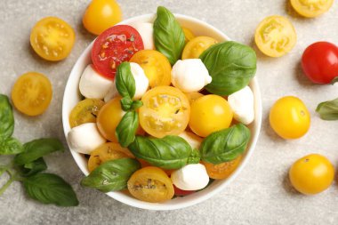 Sarı domatesli taze salata, fesleğen ve mozzarella peyniri gri masada, düz yerde.