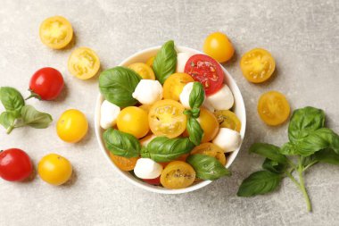 Sarı domatesli taze salata, fesleğen ve mozzarella peyniri gri masada, düz yerde.
