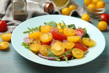 Açık mavi ahşap masada servis edilen yeşil domatesli taze salata.