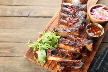 Lezzetli domuz pirzolası, roka, sos ve soğan ahşap masada, üst tarafta.