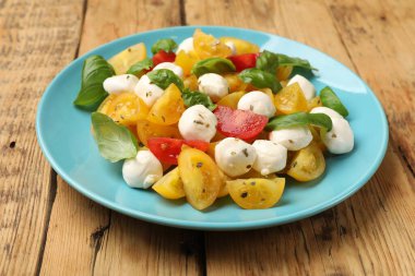 Sarı domatesli lezzetli salata, fesleğen ve ahşap masada mozzarella peyniri, yakın plan.