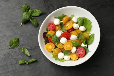 Siyah masada sarı domatesli, fesleğenli ve mozzarella peynirli lezzetli salata.