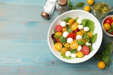 Sarı domatesli lezzetli salata, fesleğen ve mozzarella peyniri açık mavi ahşap masa, düz yatak. Metin için boşluk