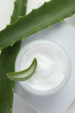 Aloe vera özütüyle nemlendirici krem ve beyaz arkaplanda yapraklar, düz bir zemin.