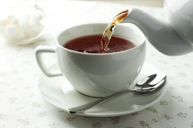 Masadaki çaydanlıktan fincana aromatik çay dökülüyor, yakın plan.