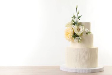 Ahşap masadaki çiçeklerle süslenmiş nefis düğün pastası beyaz arka planda. Metin için boşluk