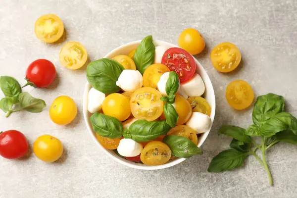 Sarı domatesli taze salata, fesleğen ve mozzarella peyniri gri masada, düz yerde.