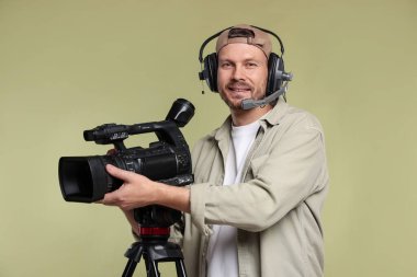 Profesyonel kamera ve soluk zeytinli arka planda kulaklığı olan bir adam.