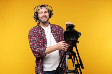 Profesyonel kamera ve turuncu arka planda kulaklığı olan bir adam.