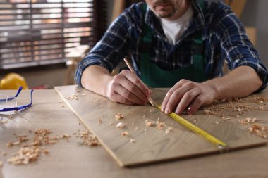 İçerideki ahşap masada bant ve kalemle tahta ölçen adam, yakın plan.