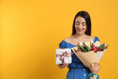 Kırmızı lale çiçeği buketi ve sarı arka planda hediye kutusu olan mutlu bir kadın. Mesaj için yer var. 8 Mart kutlamaları