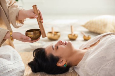 Şarkı söyleyen kadın kase terapisi görüyor. Kapalı yerde yatıyor.