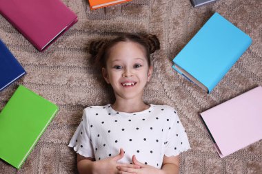 Evdeki halıda bir sürü farklı kitabı olan tatlı bir kız.