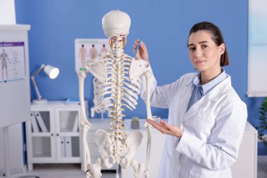 Doktor klinikteki insan iskeleti modelini işaret ediyor.