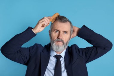 Yakışıklı bir adam açık mavi arka planda saçını tarıyor.