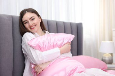 İçerde pembe ipek çarşaflarla yastığa sarılan gülümseyen kadın.