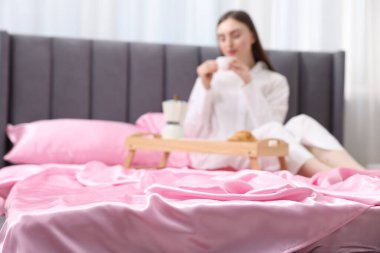 Yatakta pembe ipek çarşaflı kahve içen kadın, seçici odaklı.