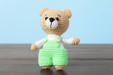 Ahşap masada açık mavi arka planda sevimli örülmüş oyuncak ayı.