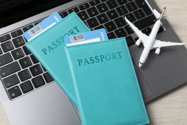 Pasaportlar, uçuş biletleri, uçak modeli ve dizüstü bilgisayar ahşap masanın üstünde.