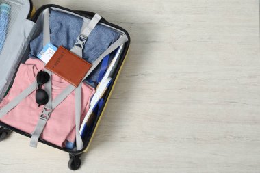 Farklı kıyafetler, pasaport ve güneş gözlükleri açık bavulda, ahşap zeminde, üst manzara. Metin için boşluk