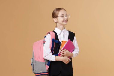 Sırt çantası ve kahverengi arka planda defterleri olan liseli kız.