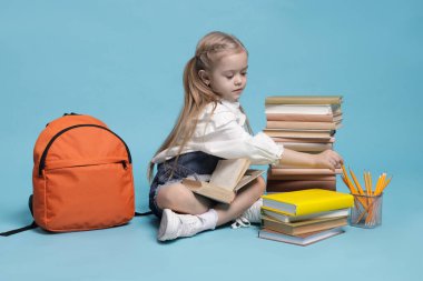 Sırt çantası ve açık mavi arka plan kitapları olan liseli kız.