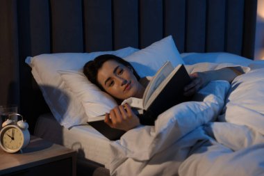 Evde yatakta kitap okuyan genç bir kadın.