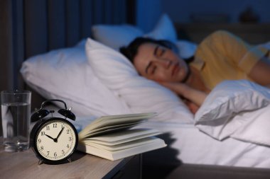 Evde uyuyan genç kadın, çalar saate ve kitaba odaklan.