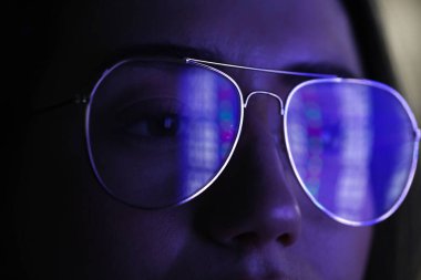 Siyah arka planda yansıması olan gözlüklü genç bir kadın, yakın plan.