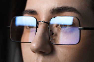 Siyah arka planda yansıması olan gözlüklü genç bir kadın, yakın plan.